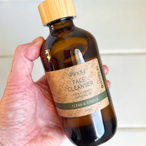 Hand holding a bottle of 'skinly' face cleanser with a wooden cap.
